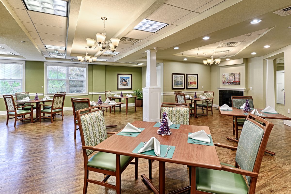 A well-lit dining area with neatly arranged tables and chairs, elegant chandeliers, and decorative elements.