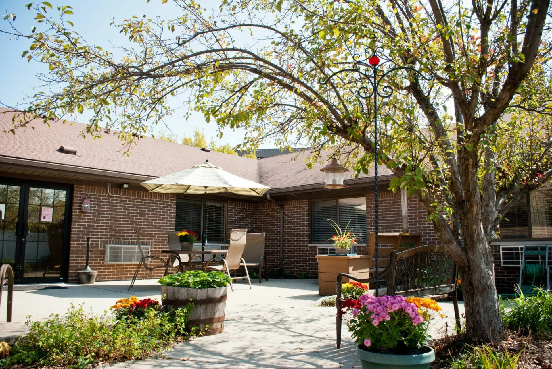 A serene patio with comfortable seating, surrounded by vibrant flowers and lush greenery.