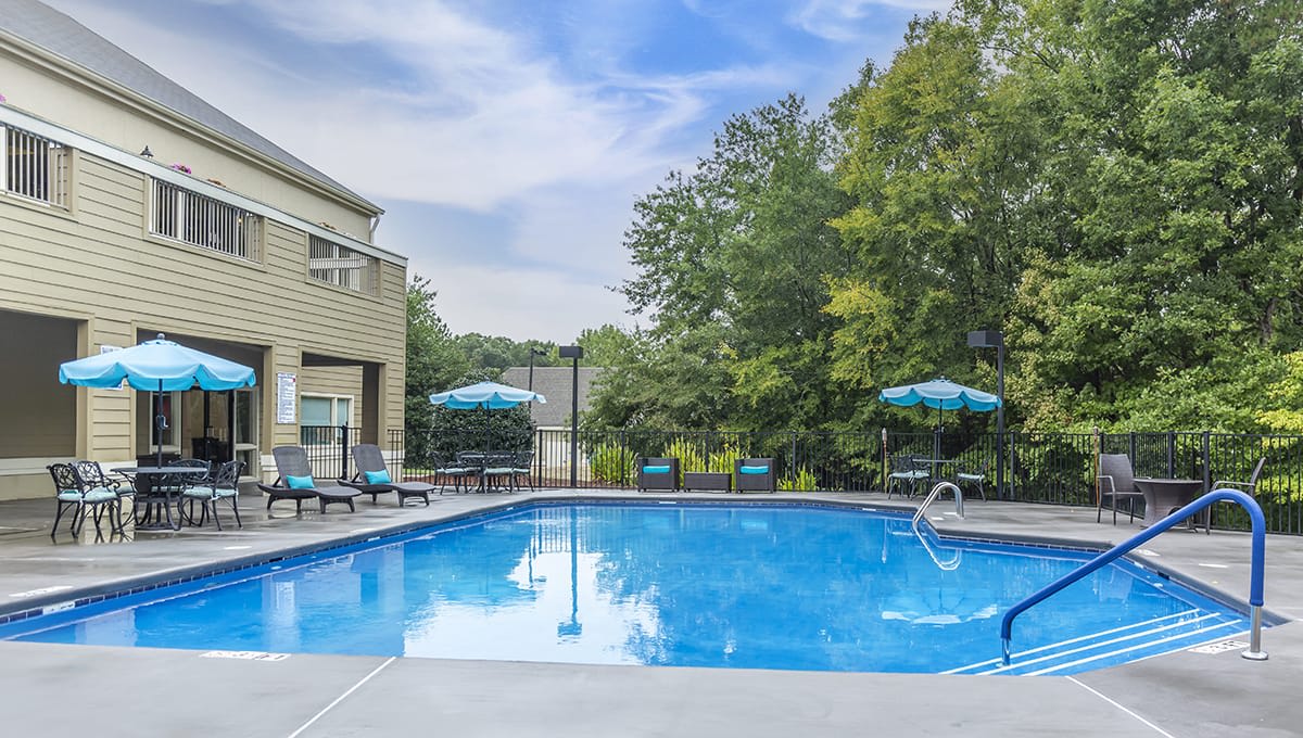 A serene outdoor swimming pool area with sun loungers and umbrellas under a clear sky.