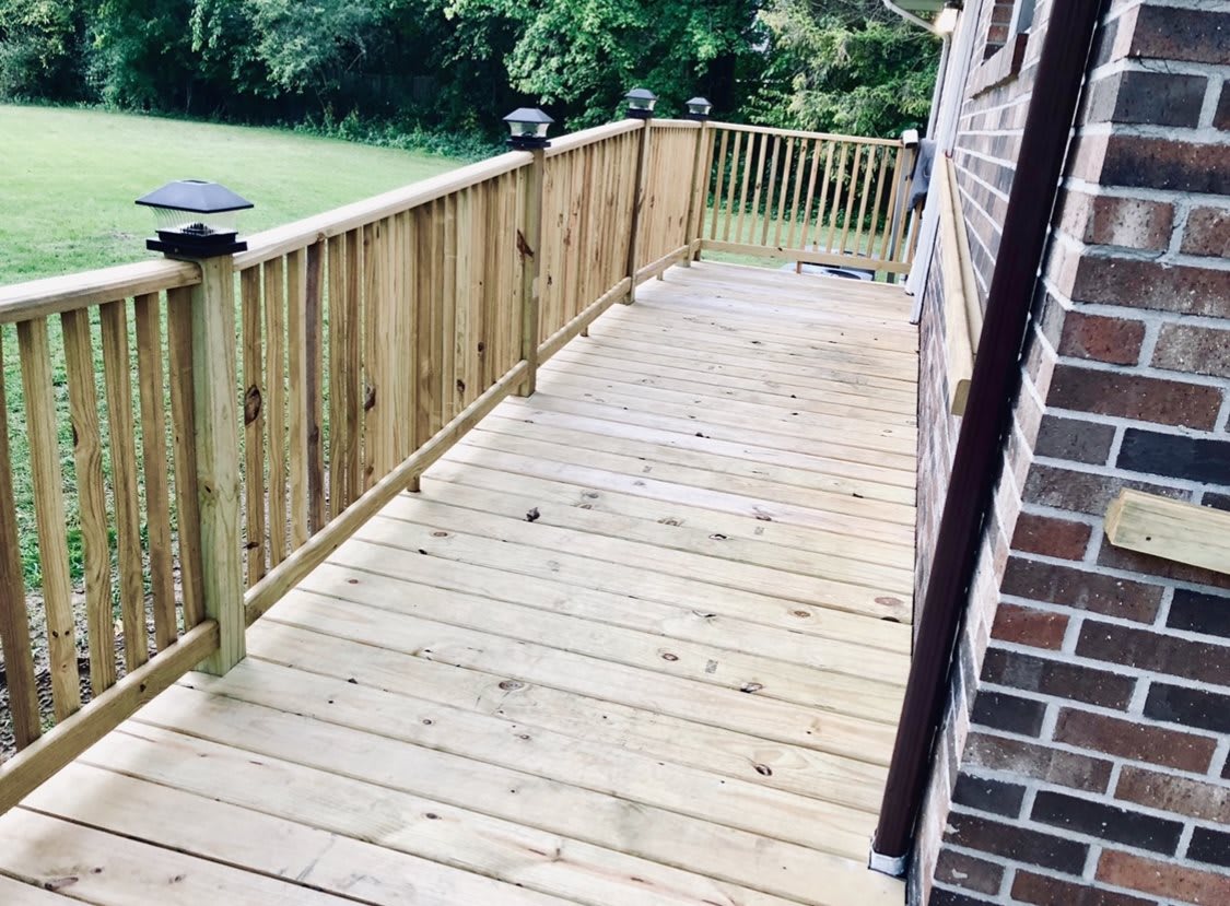 A wooden deck with a railing, adjacent to a brick wall, extends into a grassy yard.