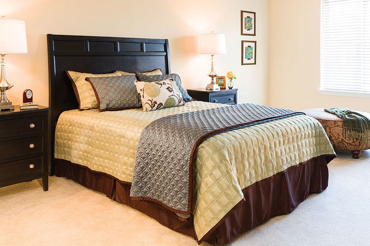 A cozy and well-decorated bedroom with a neatly made bed, featuring a patterned comforter and pillows, side tables with lamps, and wall art.