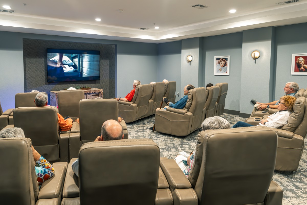 A group of elderly people enjoying a movie in a cozy home theater with recliner chairs.