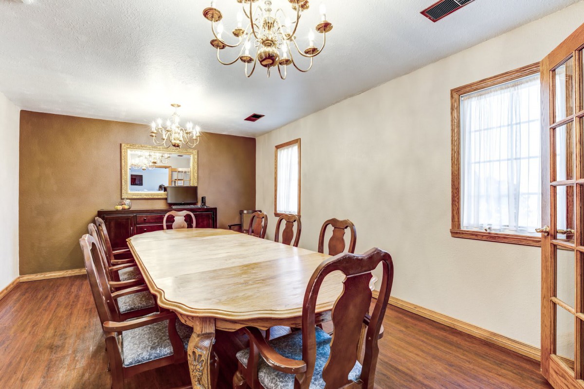 A spacious dining room featuring a large wooden table and chairs, illuminated by elegant chandeliers.