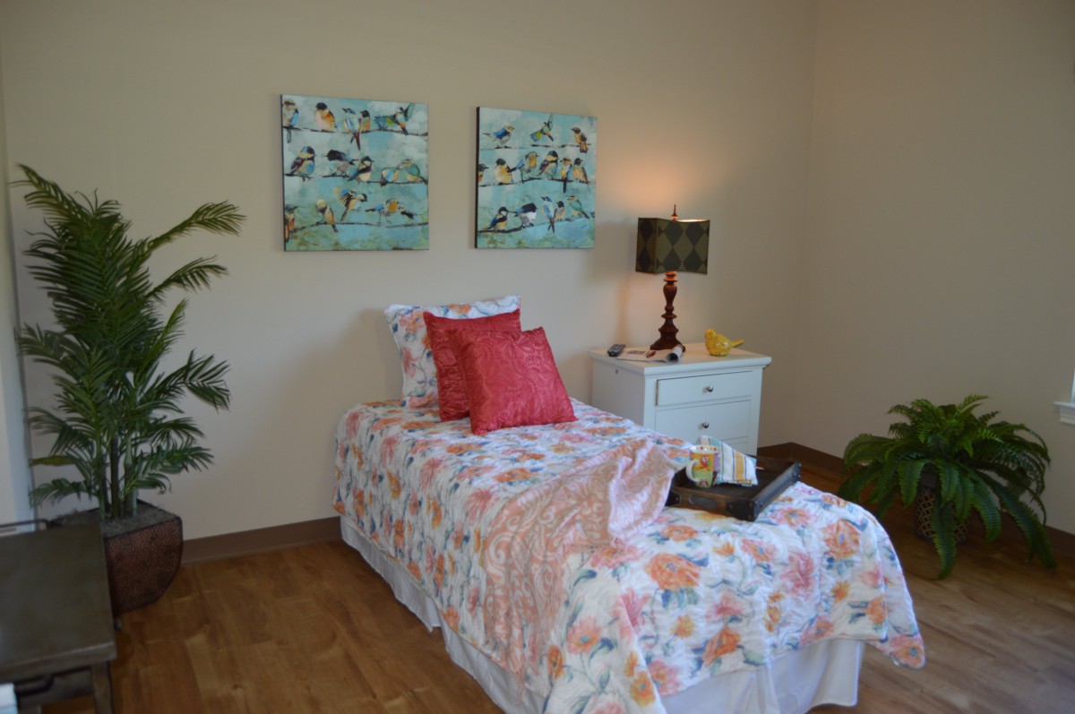 A cozy bedroom with a single bed featuring colorful bedding and decorative pillows, accompanied by a nightstand with a lamp and vibrant artwork on the walls.
