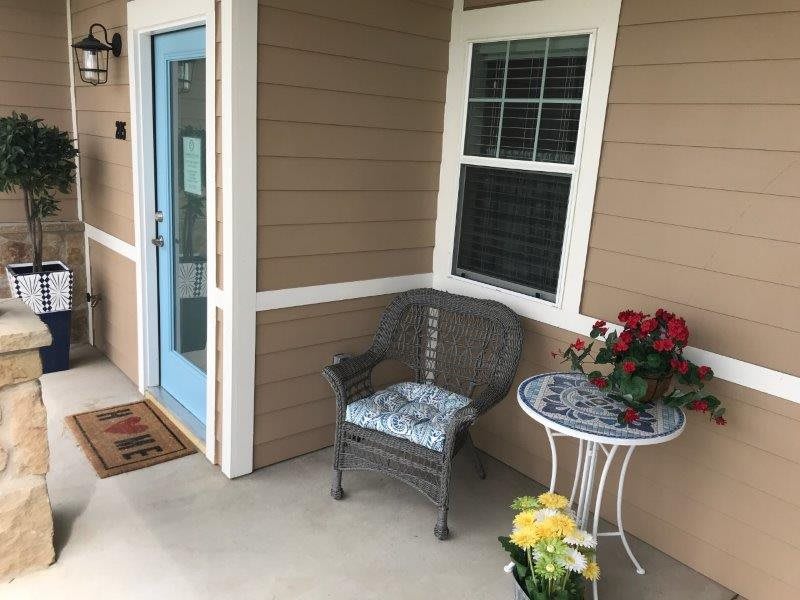 A cozy porch featuring a wicker chair, small table with flowers, and a blue door.