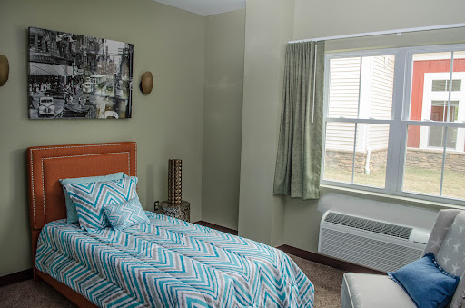 A cozy and modern bedroom featuring a single bed with a patterned quilt, a window with green curtains, and decorative wall art.