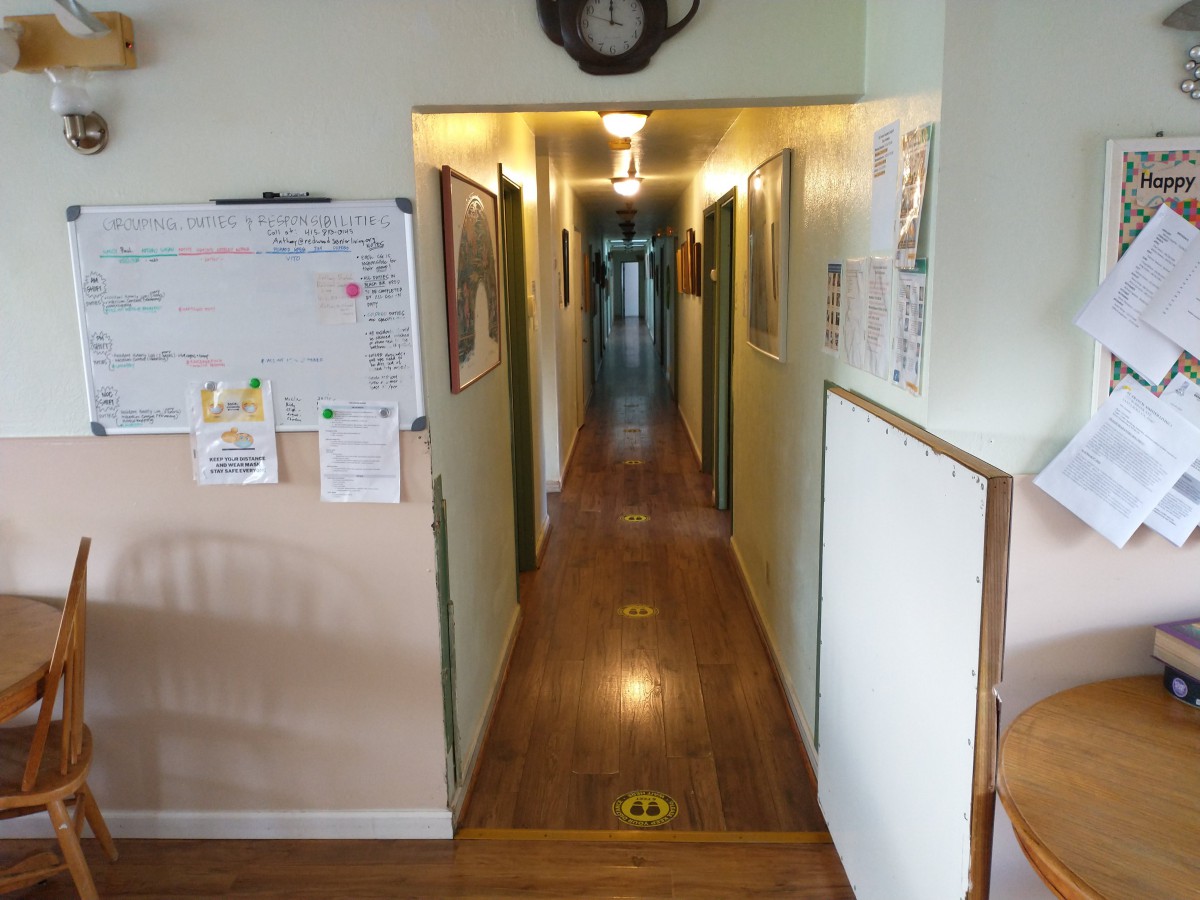 A long, narrow hallway with wooden flooring and doors along the sides, illuminated by ceiling lights.