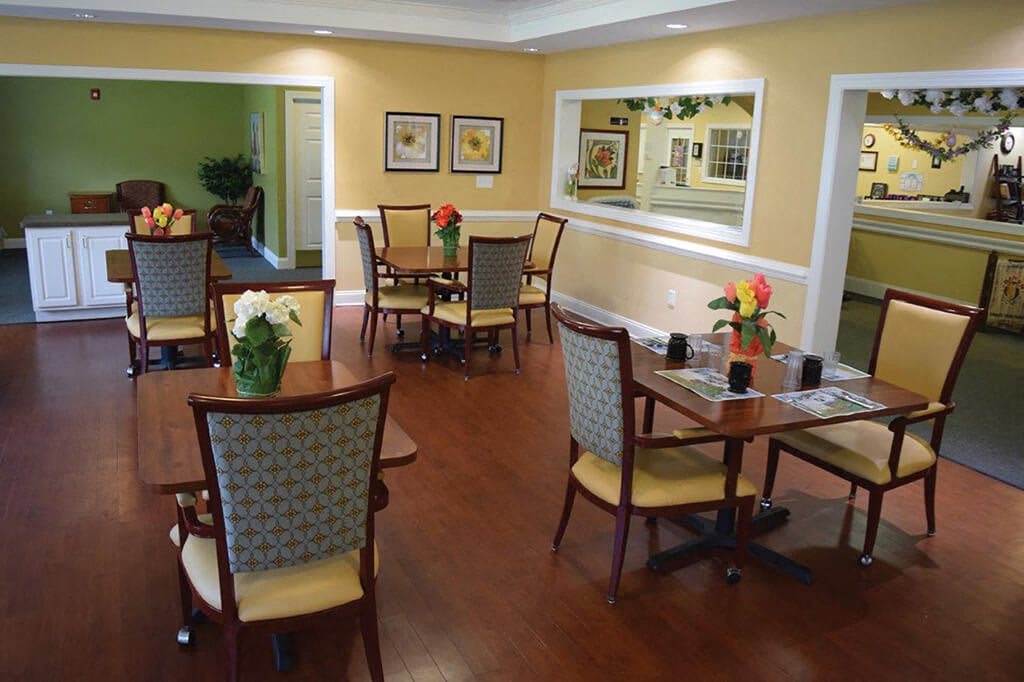 A cozy dining area with multiple tables and chairs, featuring warm yellow walls and wooden flooring.