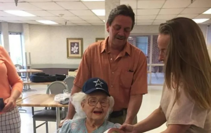 An elderly woman smiling joyfully with two people by her side, indoors.