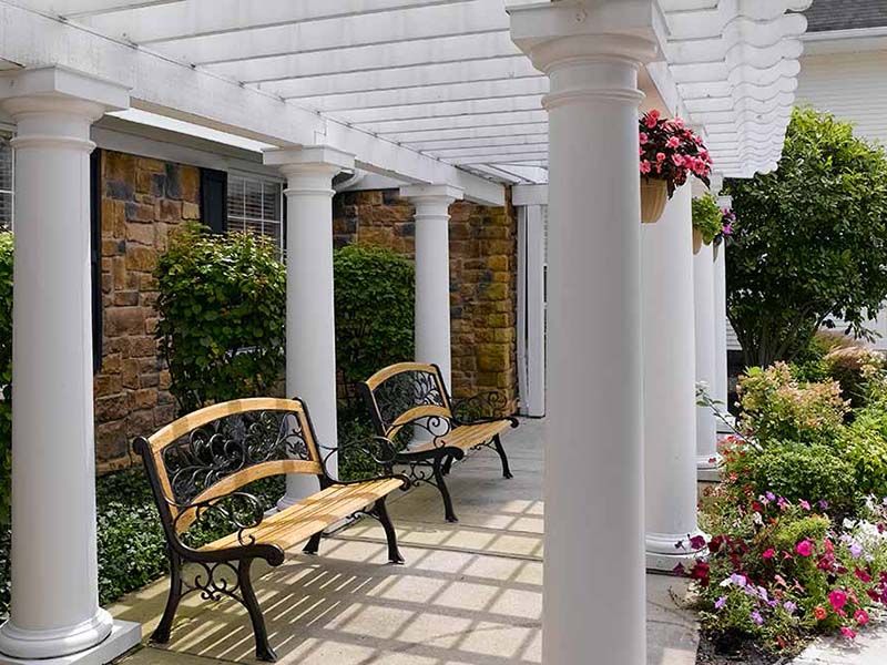 A charming outdoor patio with a pergola and benches surrounded by flowers.