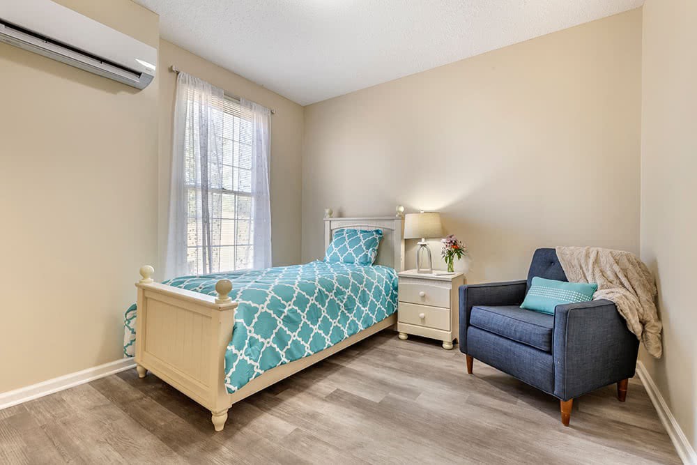 A cozy bedroom with a single bed featuring blue geometric-patterned bedding, an armchair, and a window letting in natural light.