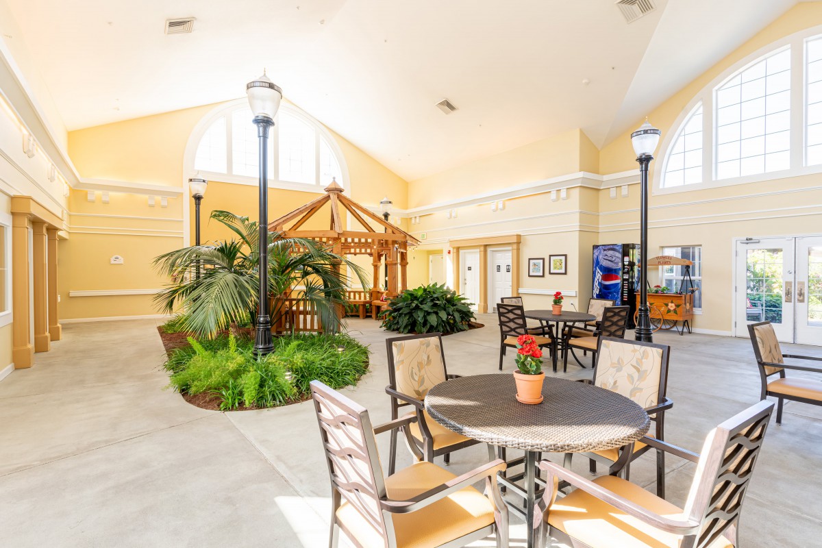 A spacious lobby with seating area, featuring tables and chairs surrounded by lush indoor plants.