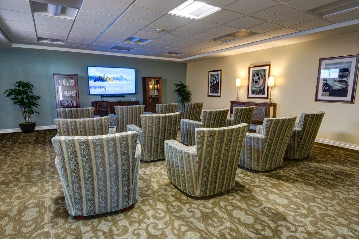 A comfortable waiting area with arranged chairs facing a television, complemented by framed art and soft lighting.