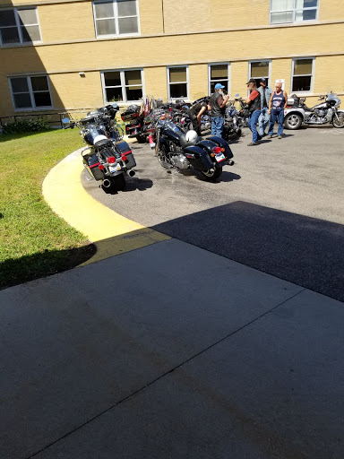 A group of bikers gathered in a parking lot on a sunny day, with their motorcycles parked nearby.