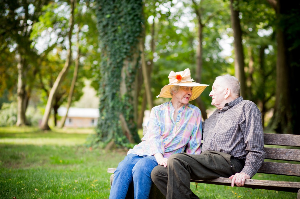 An elderly couple sitting on a bench in the park, enjoying each other's company amidst nature.