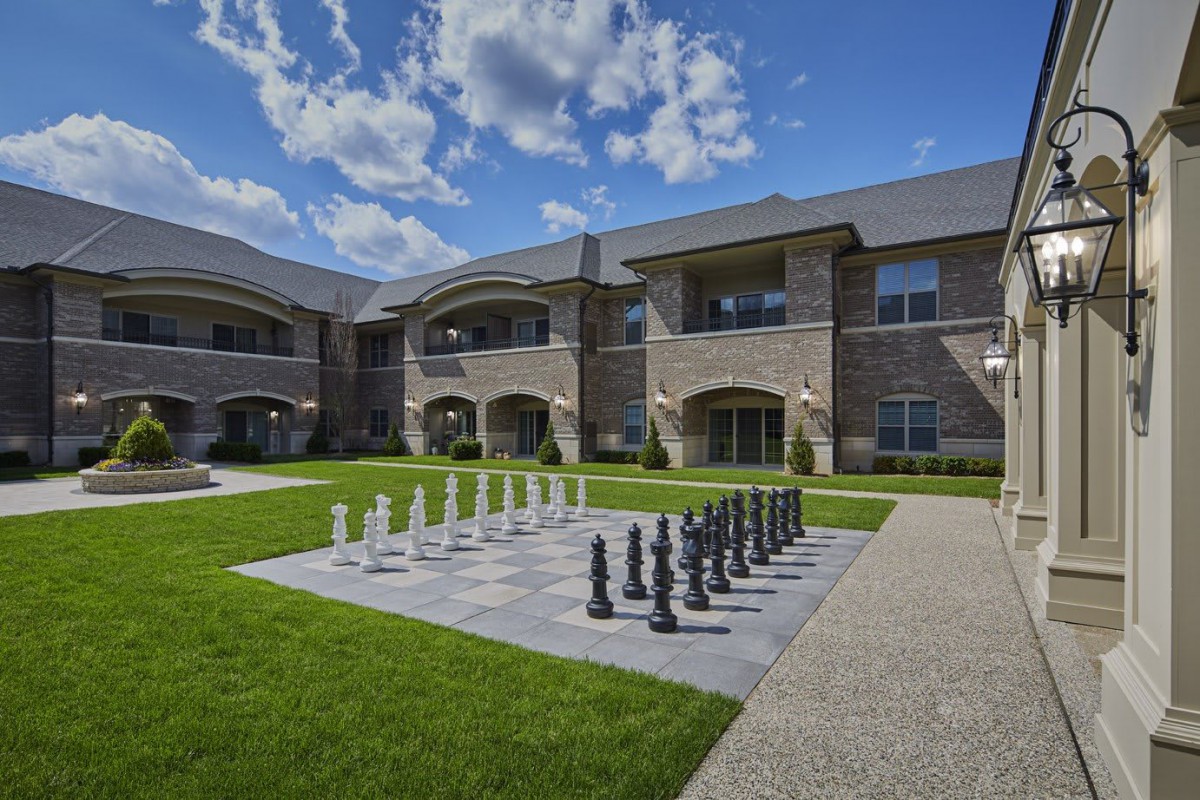 A courtyard with a large outdoor chess set in front of a brick building under a partly cloudy sky.