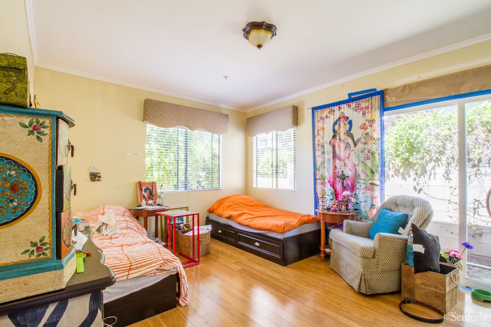 A bright bedroom with twin beds, an armchair, and a colorful tapestry.