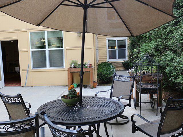 A cozy patio area with a table and chairs under an umbrella, surrounded by plants.