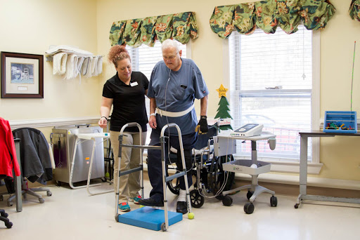 A healthcare professional assists an elderly patient with mobility training using a walker in a rehabilitation setting.