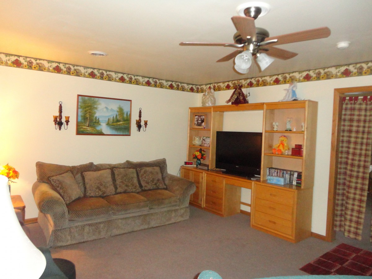 A cozy living room with a large couch, ceiling fan, and an entertainment center housing a television.