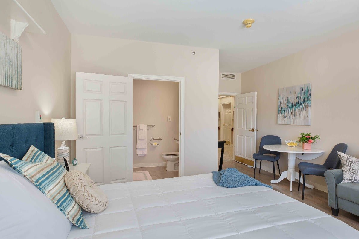 A bright and neatly arranged bedroom with a bed, desk, chair, and wall artwork.