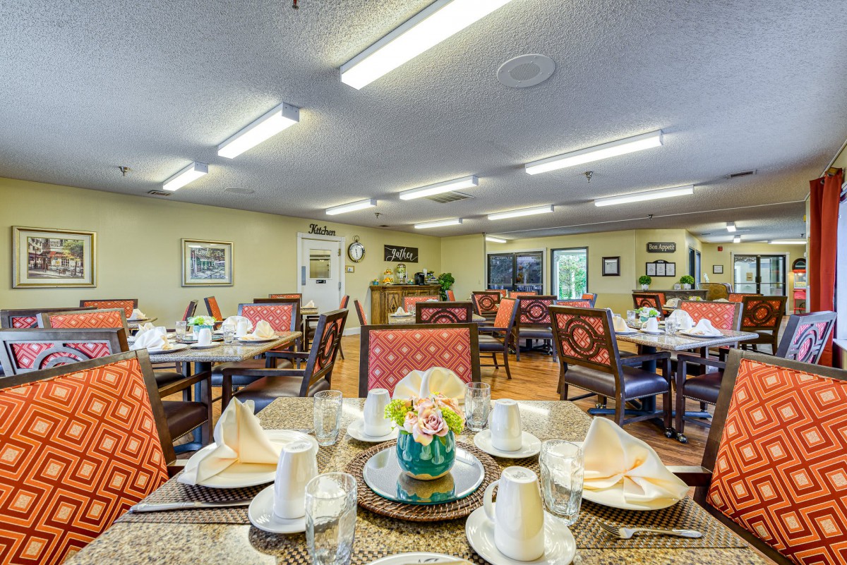 A well-arranged dining room featuring tables set with cups, napkins, and a central floral arrangement.