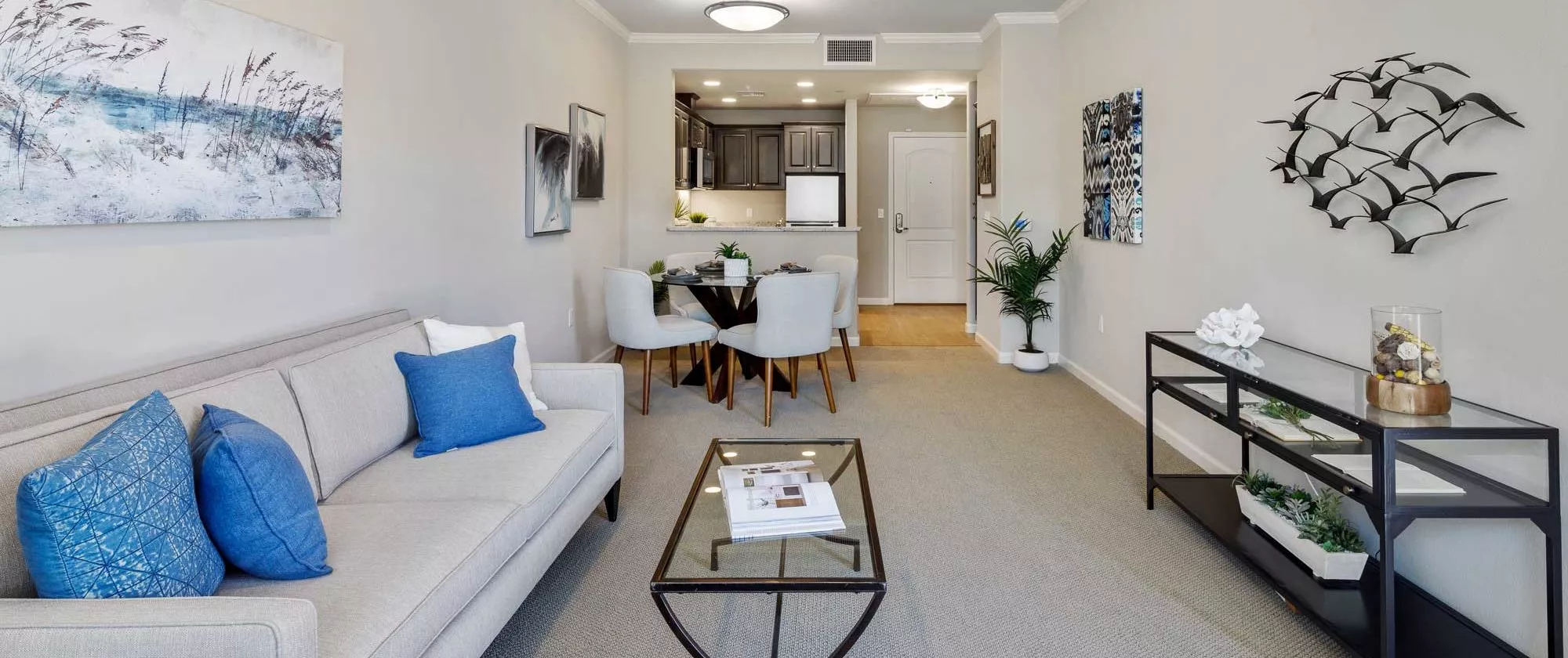 A modern apartment interior featuring a cozy living room with a coffee table, adjacent dining area, and an open kitchen.