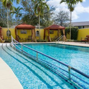 A serene outdoor swimming pool surrounded by palm trees and cabanas on a sunny day.