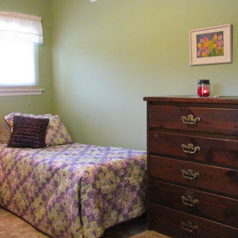 A cozy bedroom with a single bed, green walls, and a wooden dresser.