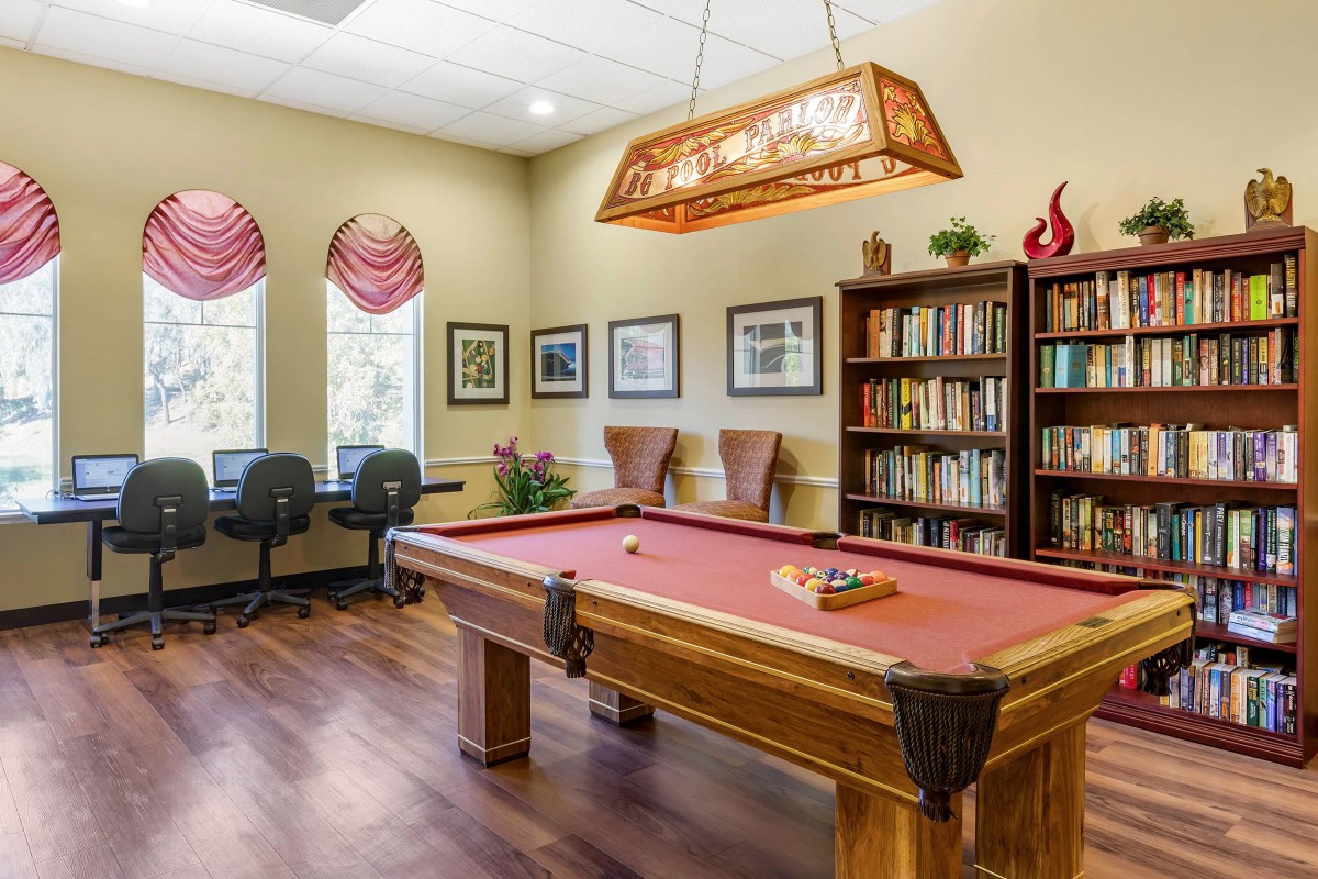 A cozy game room with a billiards table and a library with bookshelves.