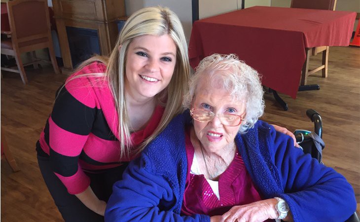 A young woman and an elderly woman smiling together indoors.