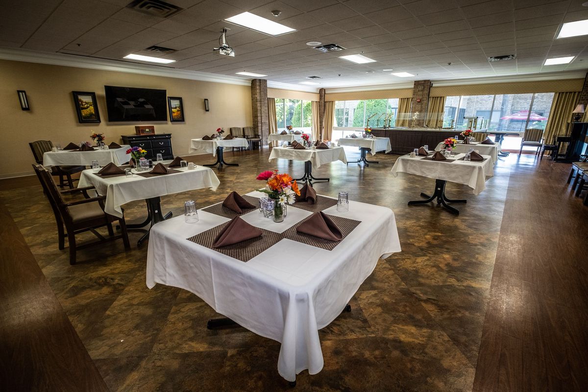A spacious dining room with neatly arranged tables covered in white tablecloths and adorned with flowers.