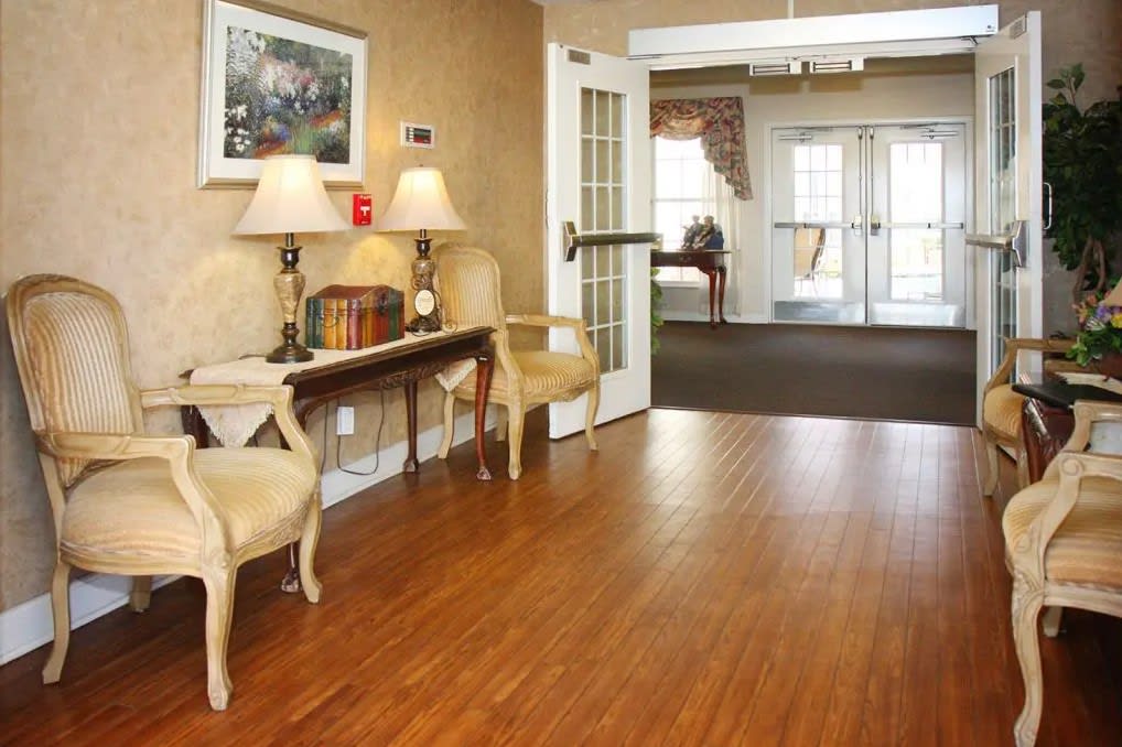 A cozy lobby area with chairs and a table adorned with lamps, leading to a bright doorway.