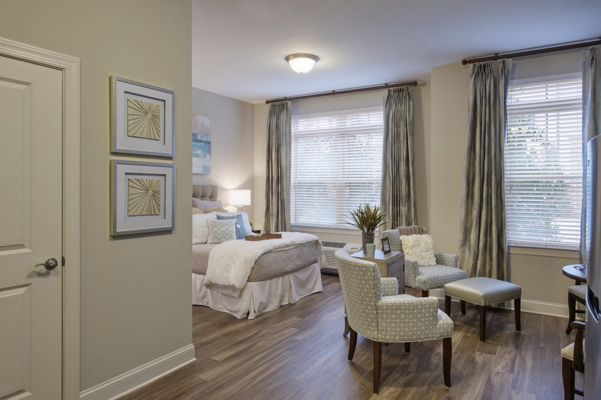 A cozy and modern bedroom with elegant decor, featuring a bed, chairs, and large windows with curtains.