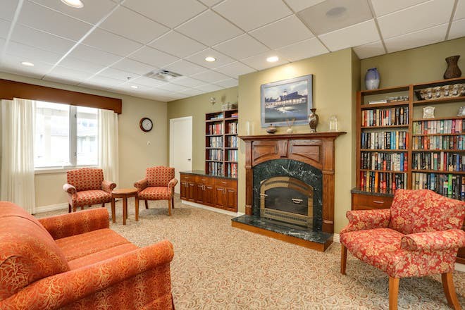 A cozy living room featuring a fireplace, surrounded by bookshelves and comfortable chairs.