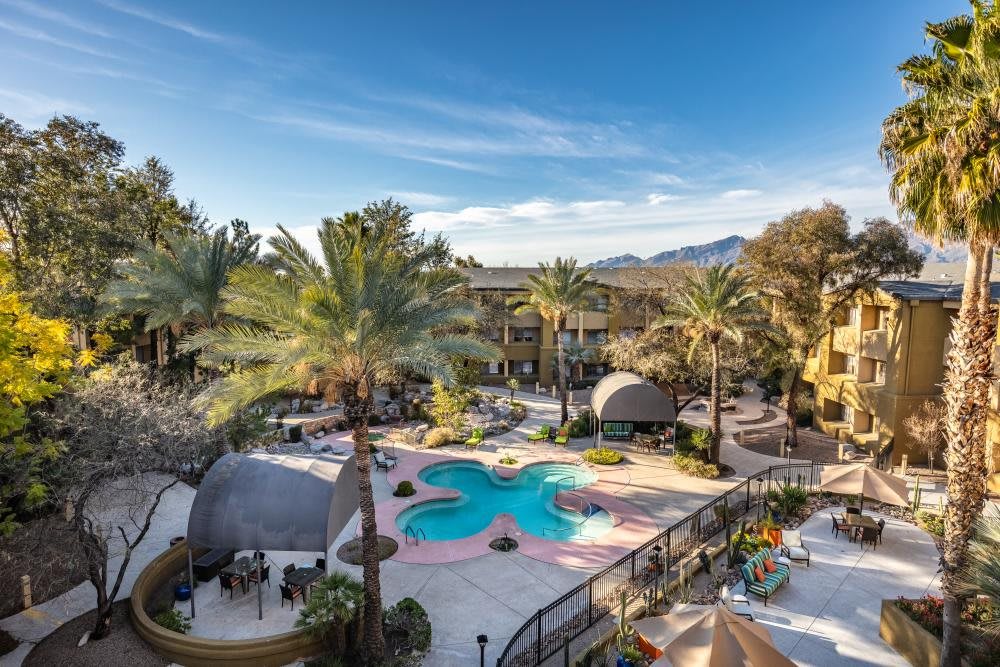A scenic view of a resort featuring a unique flower-shaped swimming pool surrounded by palm trees and lounge areas.