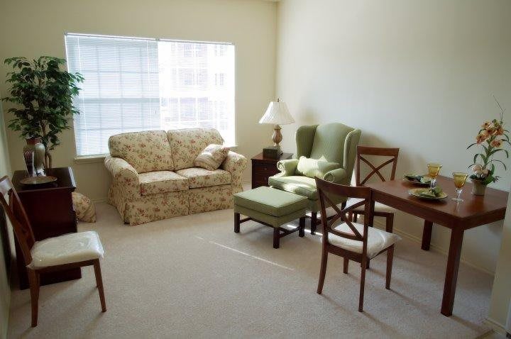 A cozy living room with a floral sofa, green armchair, and an elegant dining area.