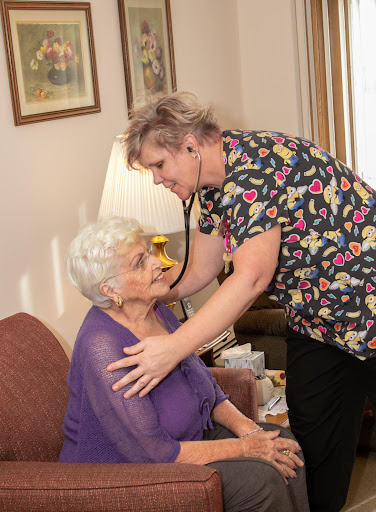 A nurse conducts a medical examination of an elderly woman at home, using a stethoscope to check her health.