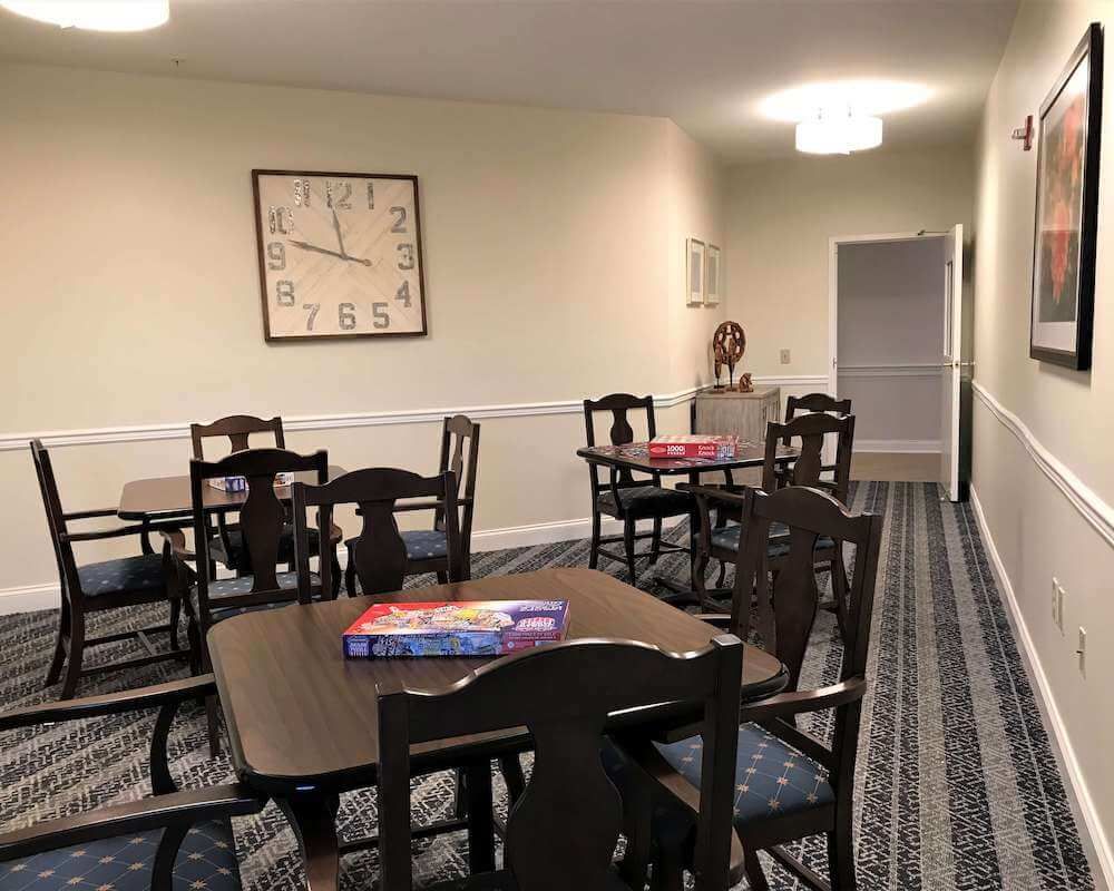 A cozy room with multiple tables and chairs, featuring a wall clock and carpeted flooring.