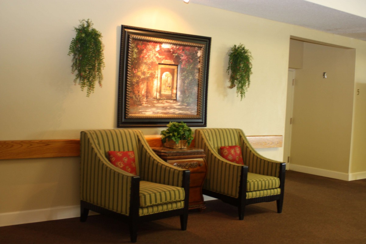 A cozy lobby area with two striped armchairs, a decorative painting, and potted plants.