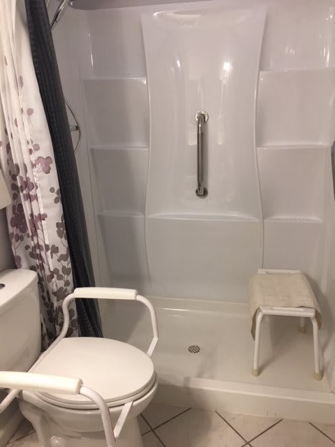 A bathroom with accessibility features including a grab bar and shower chair.