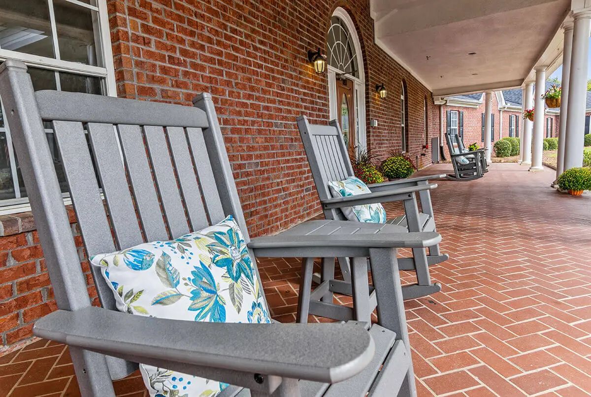 Gray rocking chairs with floral cushions line a brick porch.