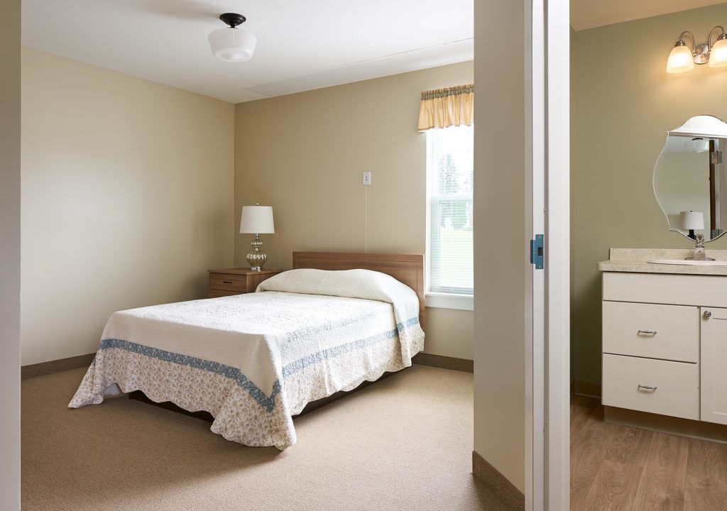 A simple and clean bedroom with a bed, lamp, and window.