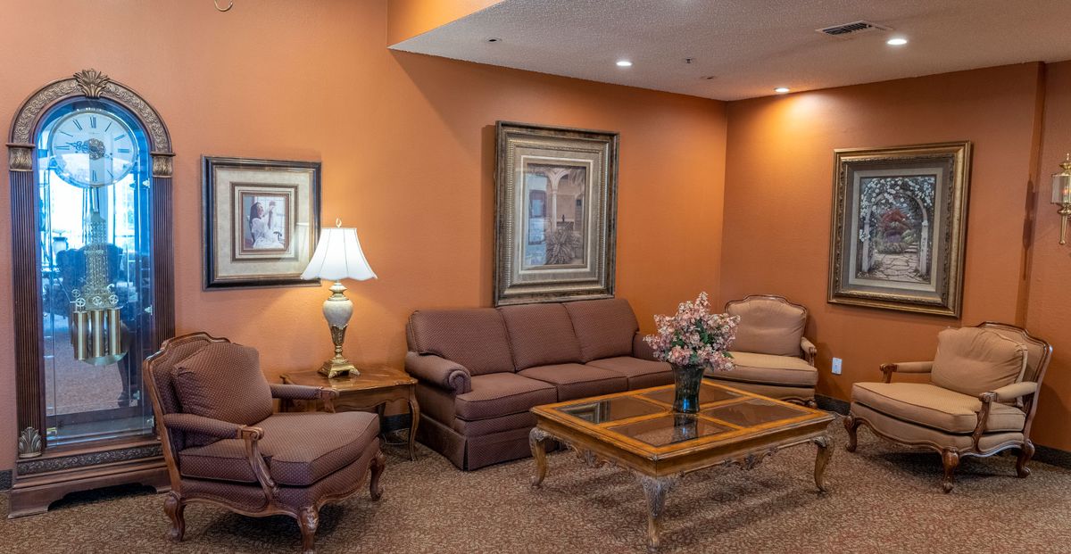 A cozy living room with warm orange walls, featuring a sofa, armchair, coffee table, lamp, and framed artwork.