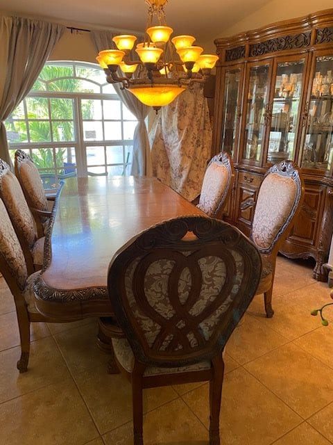 Elegant dining room with a large wooden table and upholstered chairs, illuminated by a chandelier.
