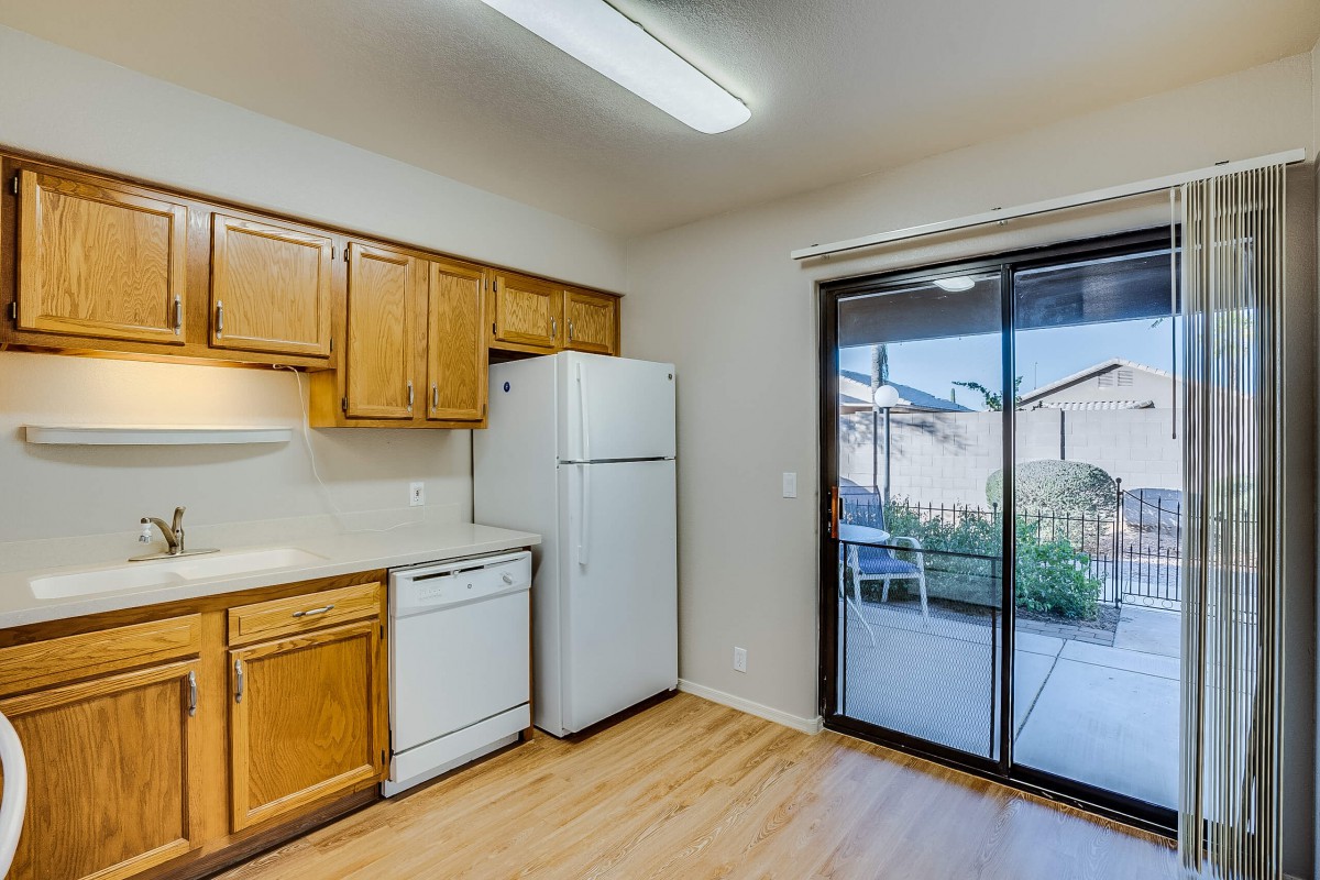 A well-lit kitchen with wooden cabinets and modern appliances, including a refrigerator and dishwasher, opens to an outdoor view through sliding glass doors.
