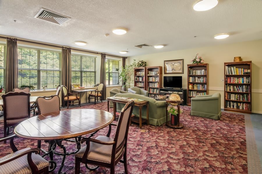 A cozy communal living space with sofas, bookshelves, and large windows.