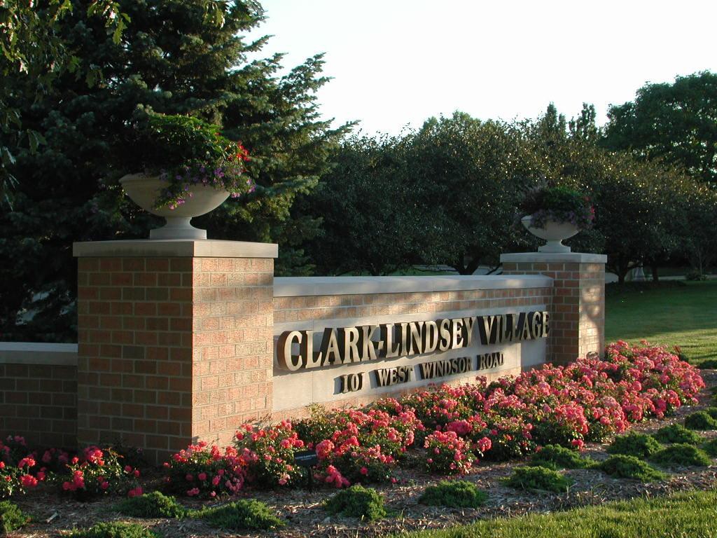 Entrance sign to Clares Garden Village surrounded by vibrant flowers and greenery.