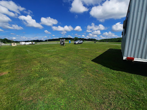 A sunny day in an open field with vehicles parked on the grass under a blue sky dotted with clouds.