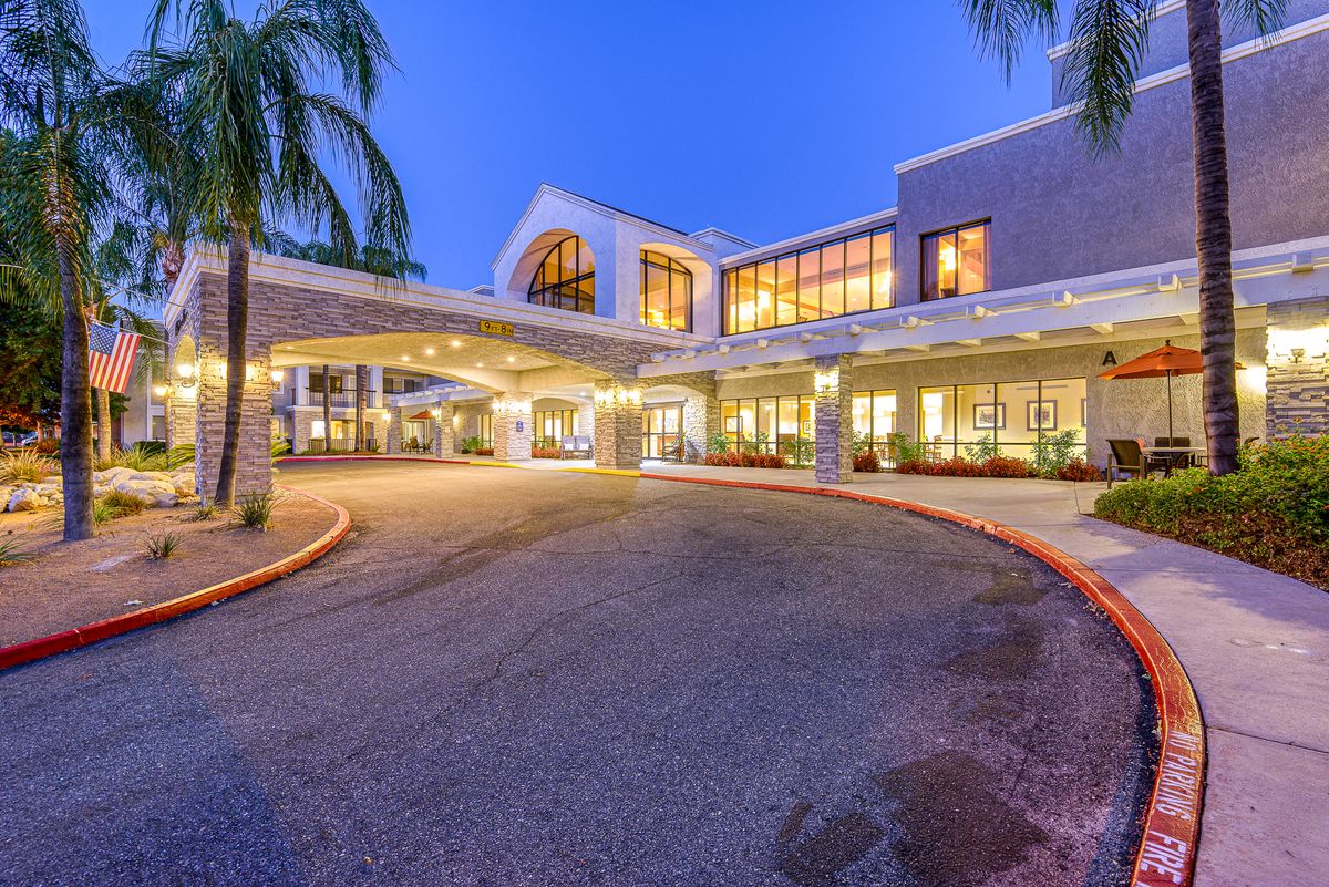 Illuminated hospital entrance with palm trees at night.